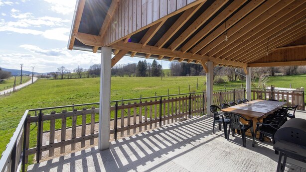 Une terrasse extérieure avec une table et des chaises en bois, un barbecue et une vue sur un champ verdoyant.