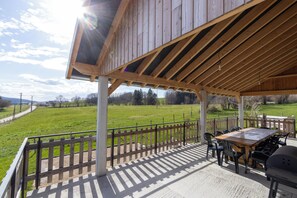Une terrasse extérieure avec une table et des chaises en bois, un barbecue et une vue sur un champ verdoyant.