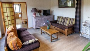 Un salon chaleureux avec un canapé, une table basse en bois et un téléviseur posé sur un meuble.