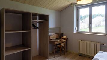 Een kamer met een houten plafond, een grote inbouwkast, een bureau met stoel, een radiator en een raam met uitzicht op bomen.