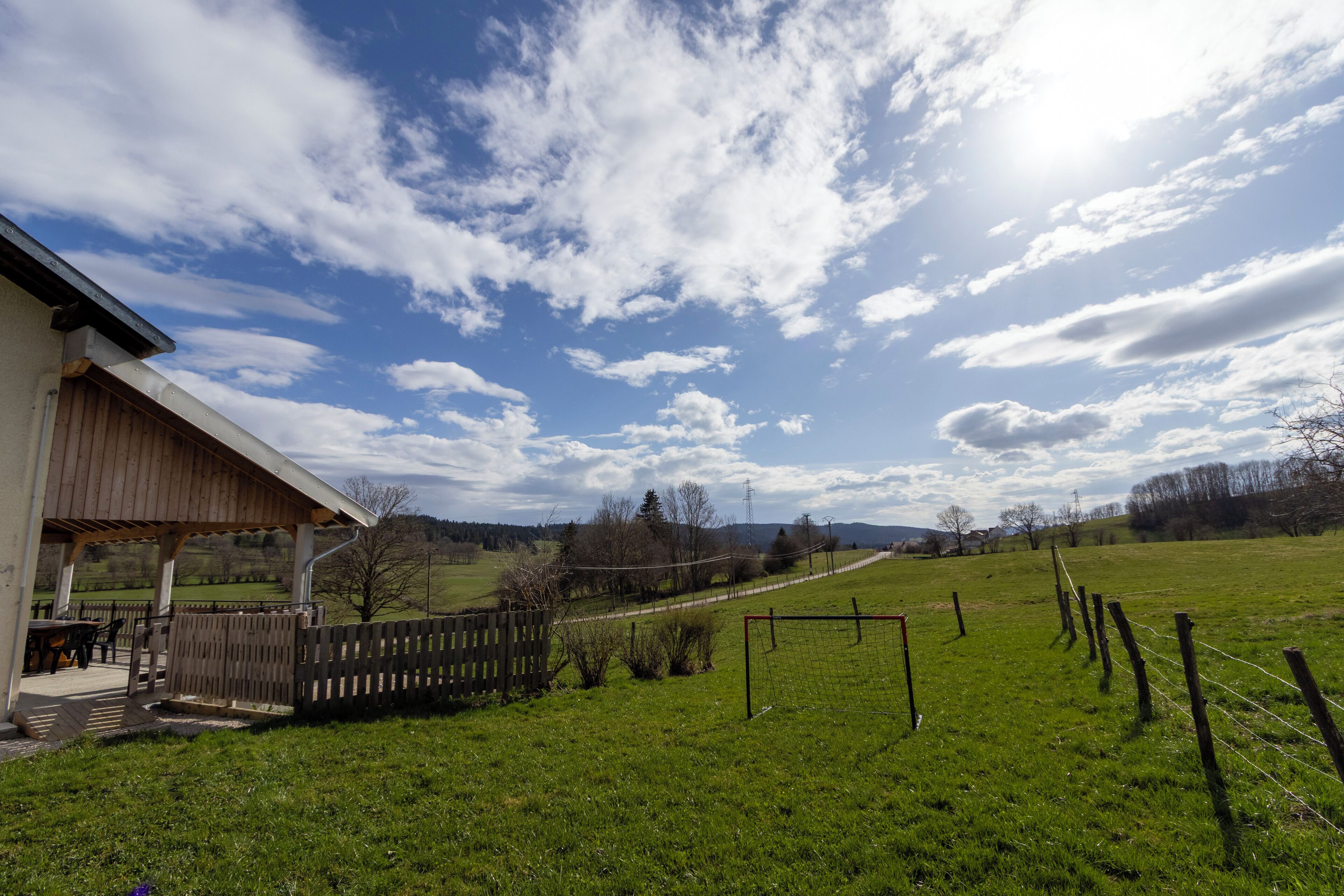 Un espace extérieur abrité, délimité par une clôture en bois, avec un terrain herbeux et un ciel dégagé.