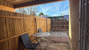 An outdoor patio area with a wooden fence, a table with chairs, and a view of a building in the background.
