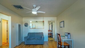 A spacious living area with a ceiling fan, a couch, a dining table with chairs, and a kitchen in the background.