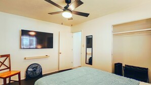 A bedroom with a bed, a ceiling fan, a TV, a chair, a wardrobe, and a mirror.