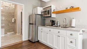 Una cocina moderna con armarios blancos, un refrigerador de acero inoxidable, un microondas y un estante de madera sobre la encimera.