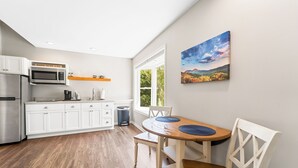 Una cocina moderna con armarios blancos, un refrigerador de acero inoxidable y un microondas. Hay una mesa de comedor con individuales azules y sillas blancas.