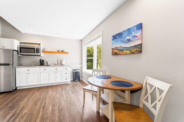 Una cocina moderna con armarios blancos, un refrigerador de acero inoxidable y un microondas. Hay una mesa de comedor con individuales azules y sillas blancas.