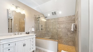 Un baño moderno con un espejo grande, un tocador con cajones, una bañera y una zona de ducha.