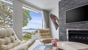 Un salon moderne doté d’une cheminée, d’une grande fenêtre offrant une vue sur la mer et d’un coin salon confortable.