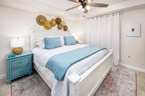 Une chambre à coucher comprenant un lit, une table de chevet, un ventilateur de plafond et un mur décoré de chapeaux.
