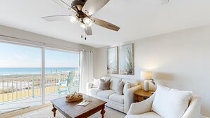 A spacious living room with a balcony overlooking the beach, a ceiling fan, and a white sofa. - Pelican Isle 117 (Fort Walton Beach)