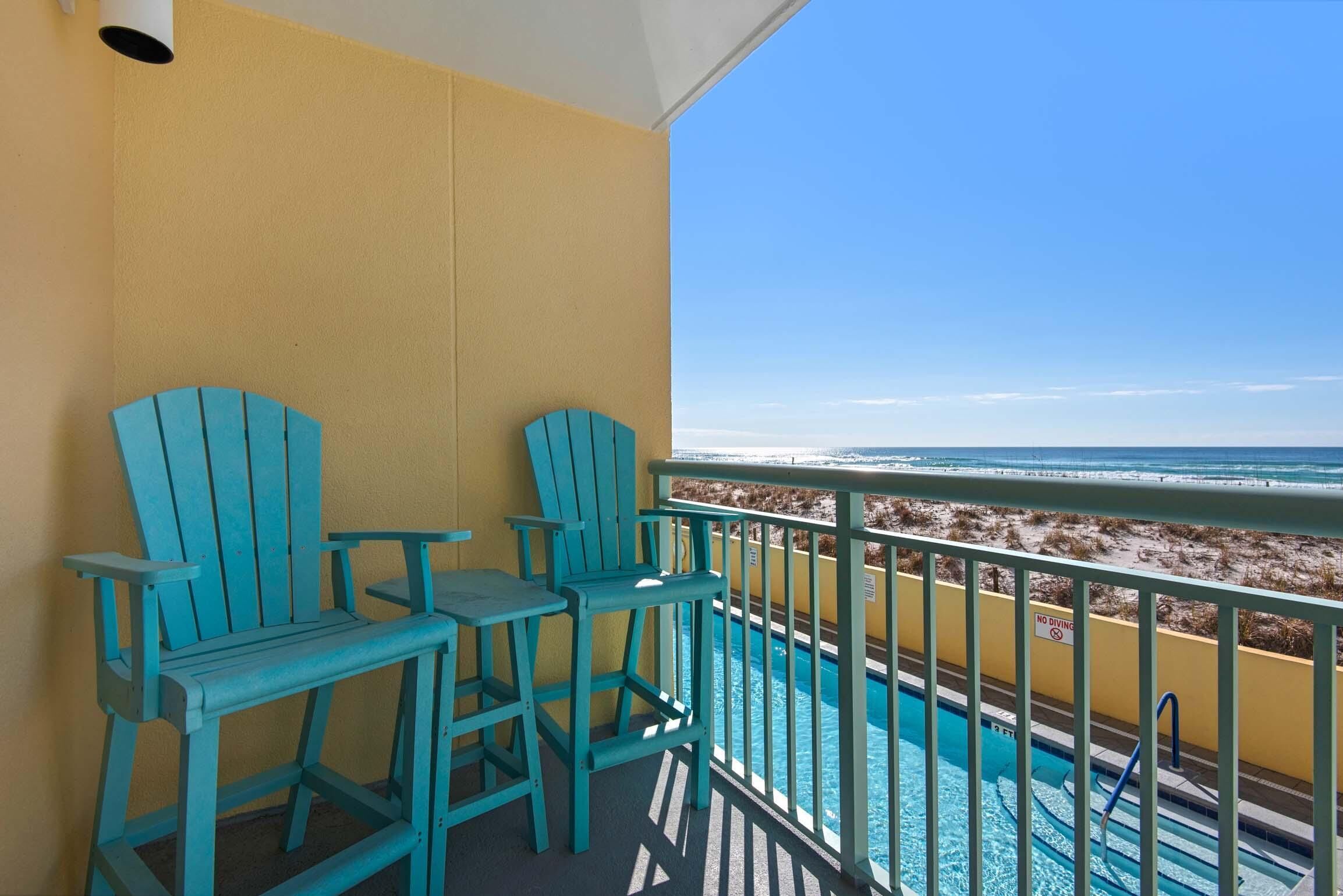 A balcony with turquoise Adirondack chairs and a pool.