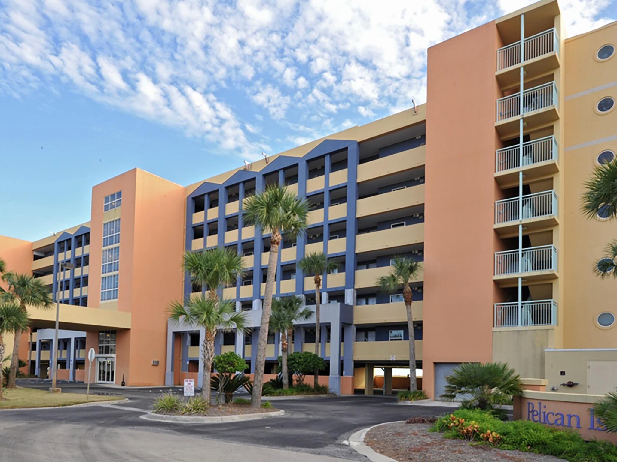 A multi-story hotel with a central atrium, palm trees, and a clear sky.