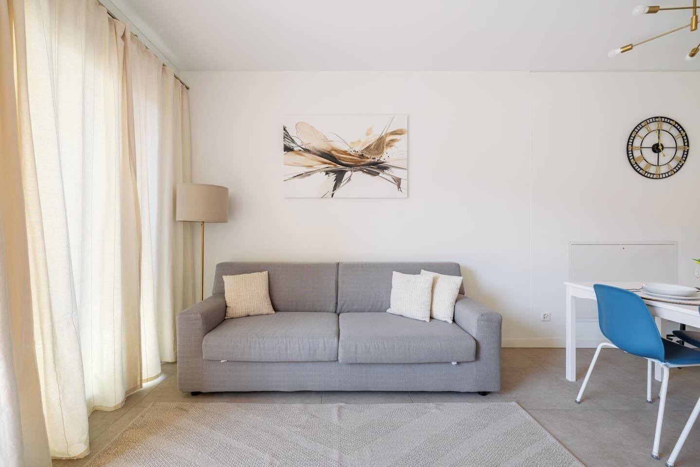 Ein modernes Wohnzimmer mit einem grauen Sofa, einer weißen Lampe, einem blauen Sessel und einer Wanduhr.