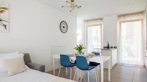 A modern bedroom with a bed, a desk, and chairs. There is a clock on the wall and a window with curtains. - Cozy & Modern Flat for 6 people / Free Parking (Lugano)