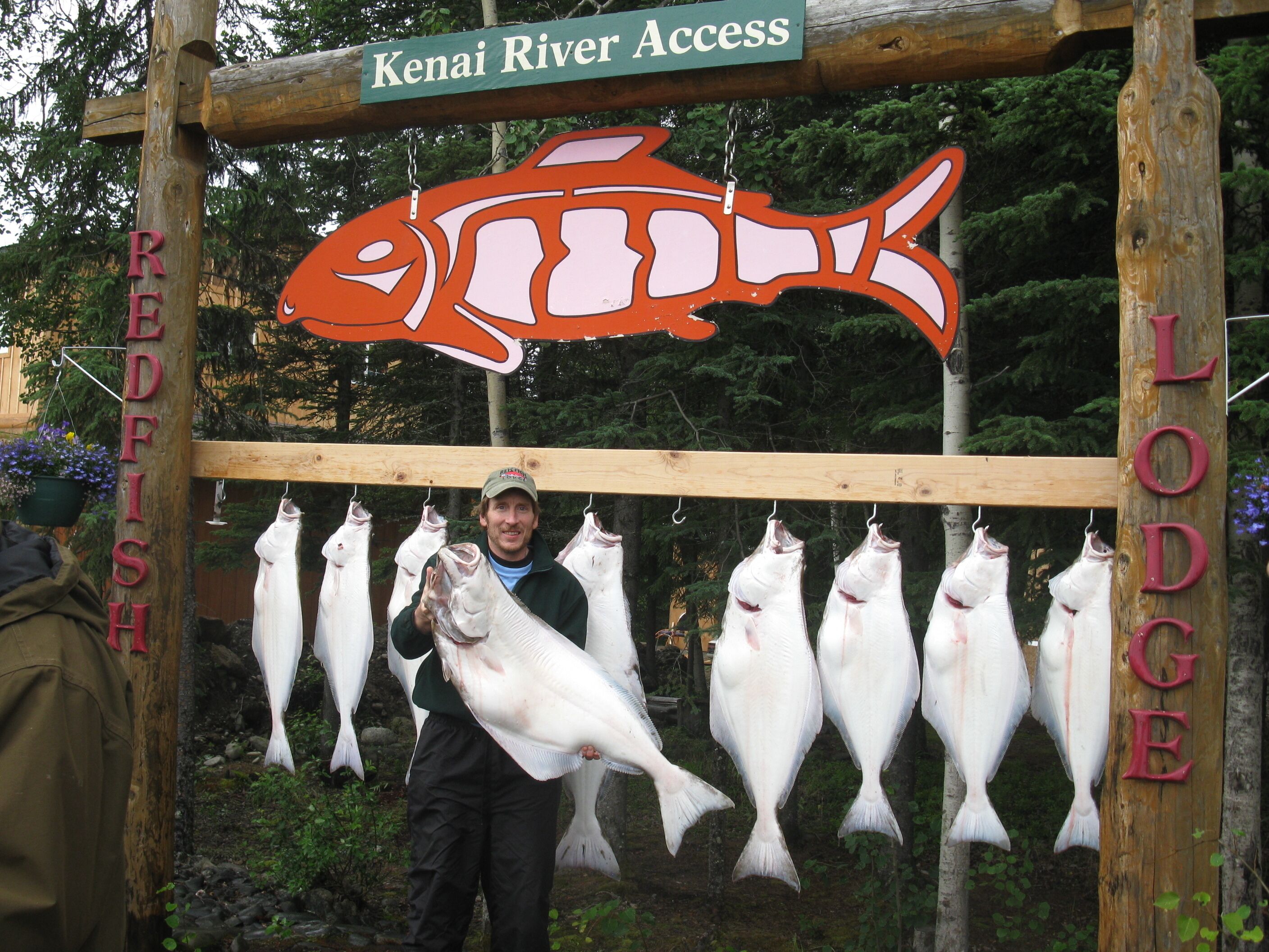 A wooden sign with a fish illustration and the words "Kenai River Access" and "Lodge" indicating a fishing area.