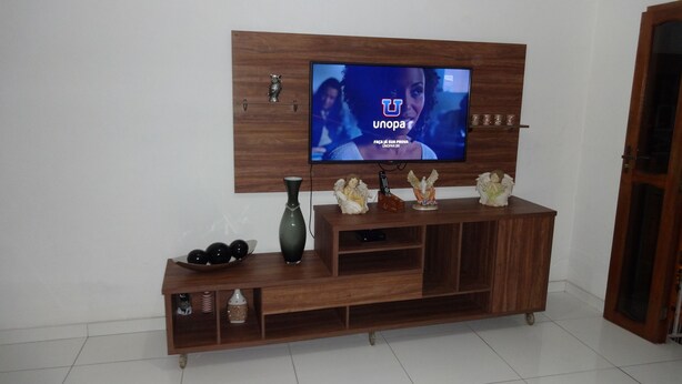 Un meuble de rangement en bois pour appareils multimédias, avec un téléviseur à écran plat fixé au mur, un vase et de petites figurines d’anges décoratives.