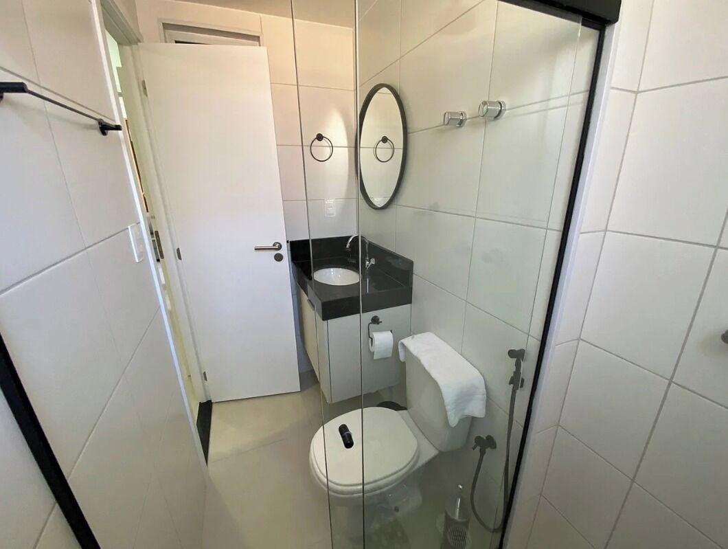Un baño compacto con cabina de ducha de vidrio, inodoro blanco, lavamanos con encimera negra y espejo sobre el lavamanos.