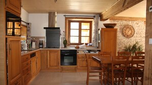 A kitchen with wooden cabinets, a stove, and a dining area with wooden chairs and a table. - Gîte 'La Valentine', secluded country house in the heart of nature (Le Barboux)