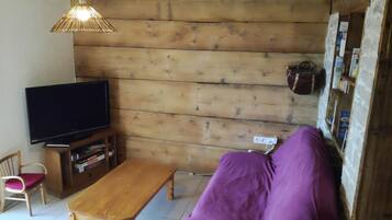 A wooden-paneled room with a television on a wooden stand, a purple sofa, a wooden table, and a wicker basket on the wall.