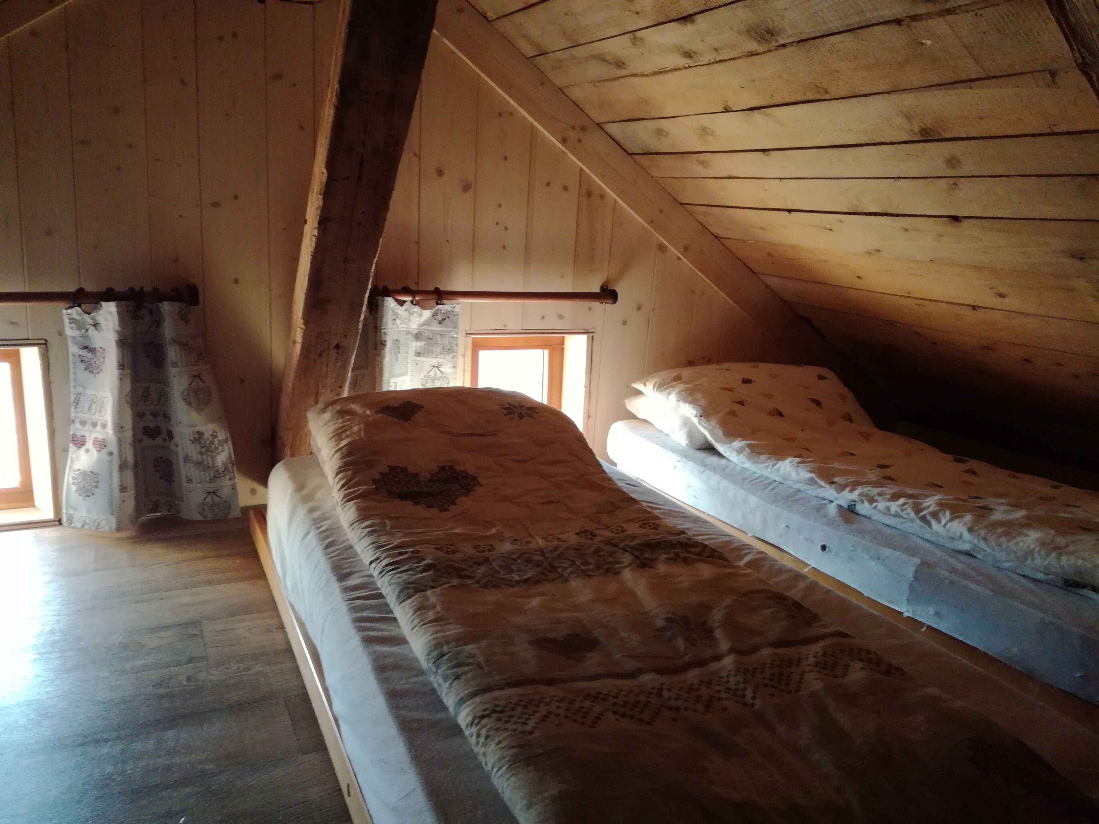 A small attic bedroom with two single beds, wooden walls, and a sloped ceiling.