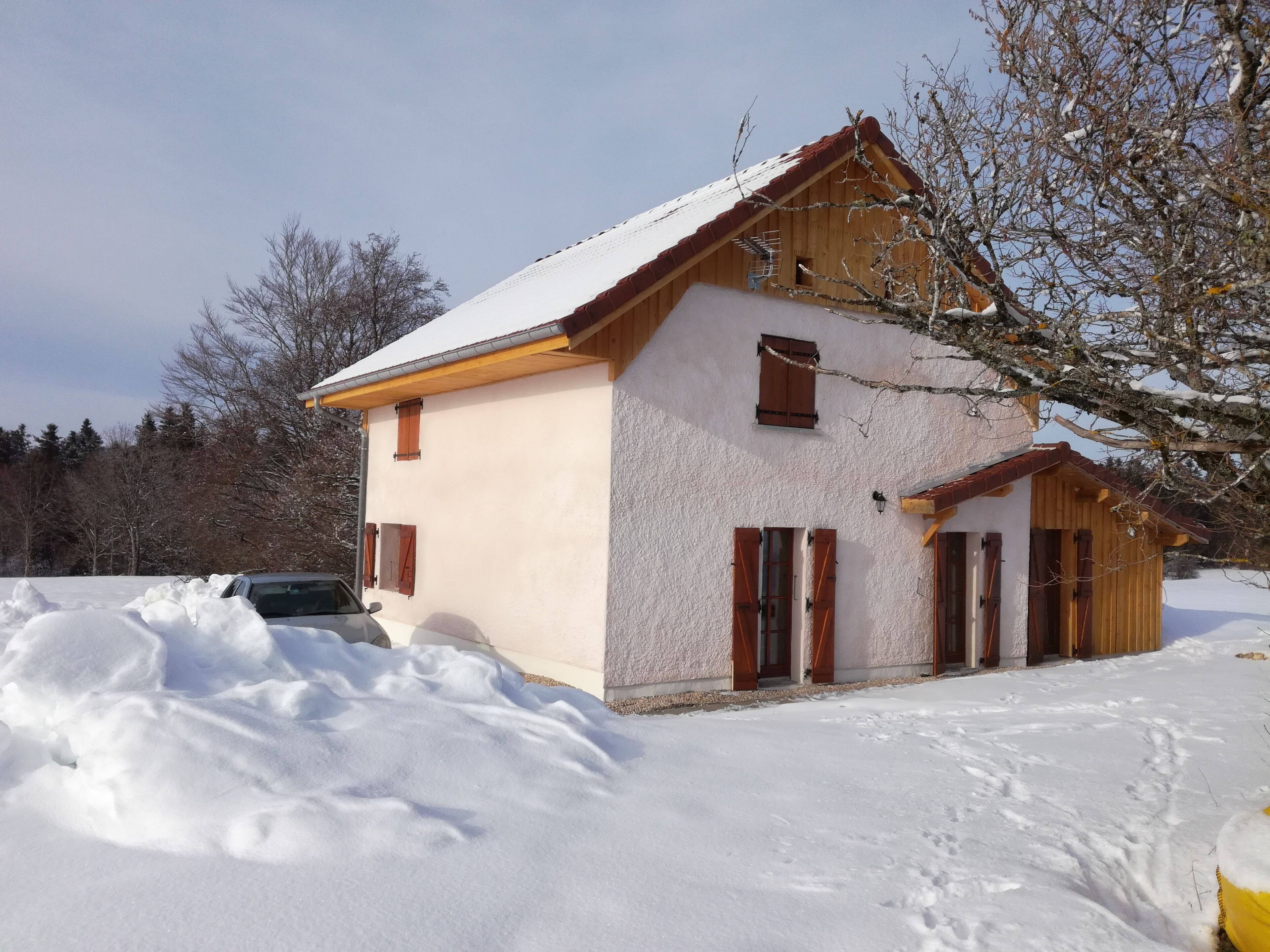 A two-story house with a sloped roof and wooden shutters, surrounded by snow.