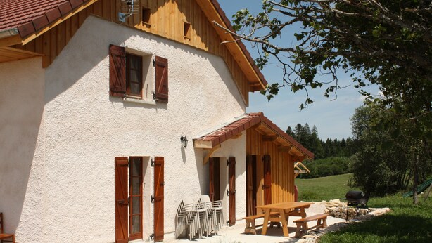 A rustic chalet with a wooden balcony, a stone patio, and outdoor seating. - Gîte 'La Valentine', secluded country house in the heart of nature (Le Barboux)