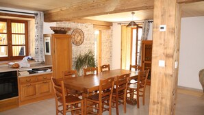 A wooden dining table with chairs, a stone wall, and a clock. - Gîte 'La Valentine', secluded country house in the heart of nature (Le Barboux)