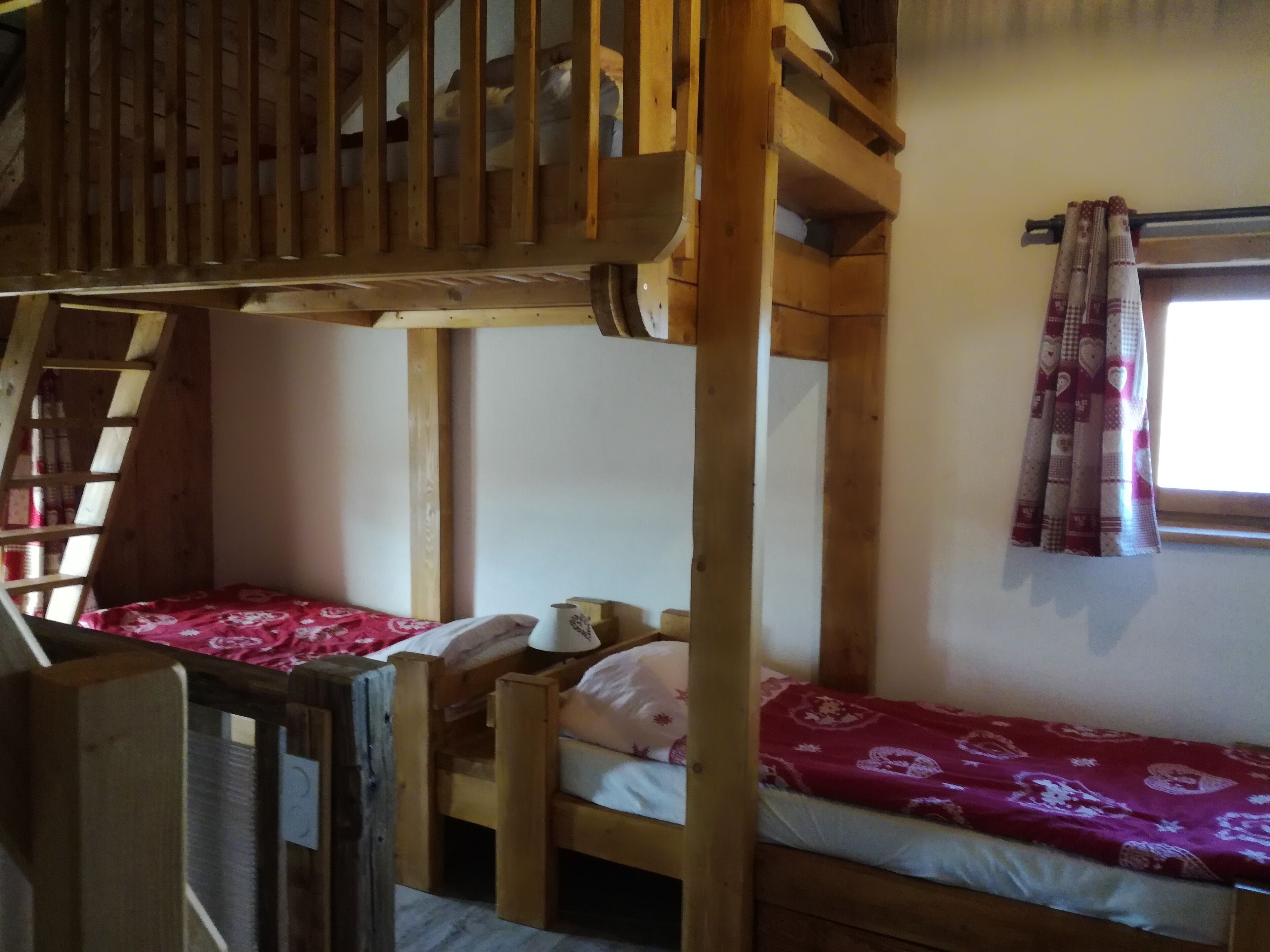 Quarto com beliche, vigas de madeira, janela com cortinas estampadas e escada.