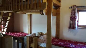 Quarto com beliche, vigas de madeira, janela com cortinas estampadas e escada.