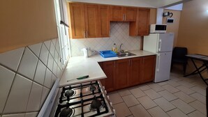 A compact kitchen with wooden cabinets, a gas stove, a microwave, and a refrigerator.