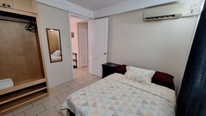 A bedroom with a bed, a wardrobe, a mirror, and an air conditioning unit.