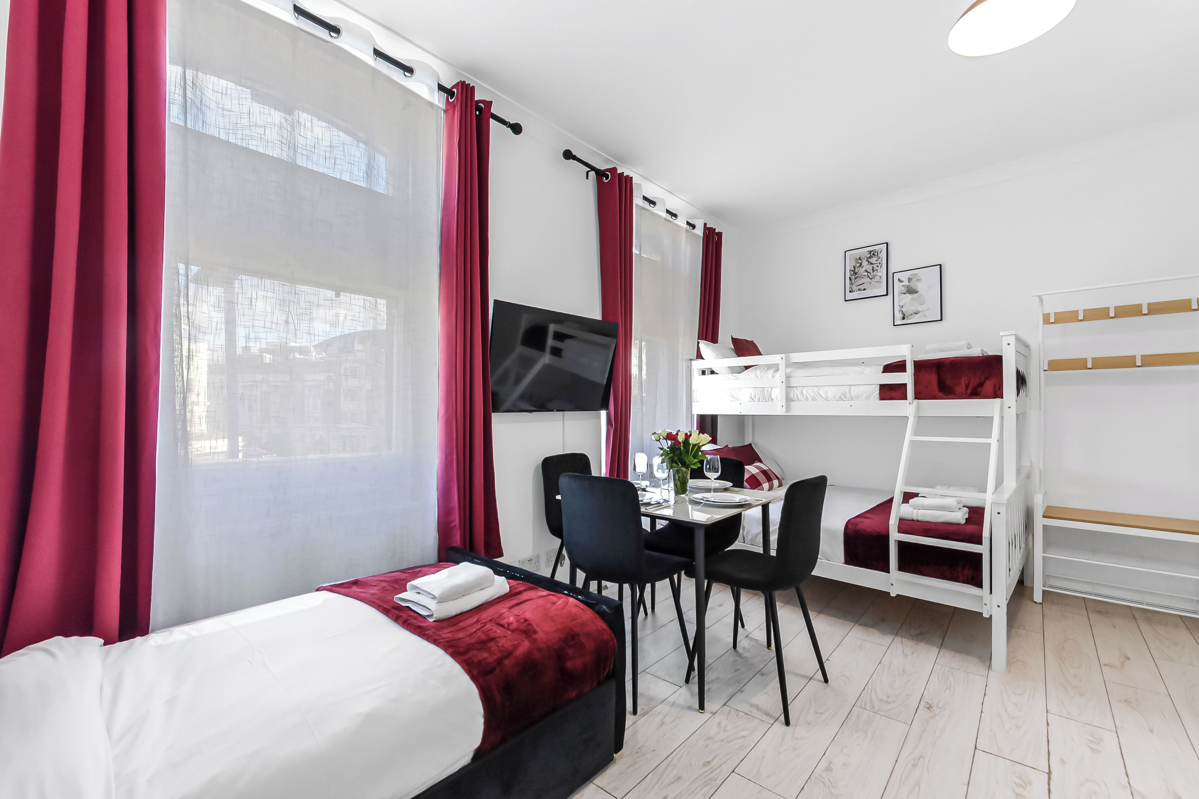 Un dormitorio con cama, escritorio, sillas, litera y cortinas.
