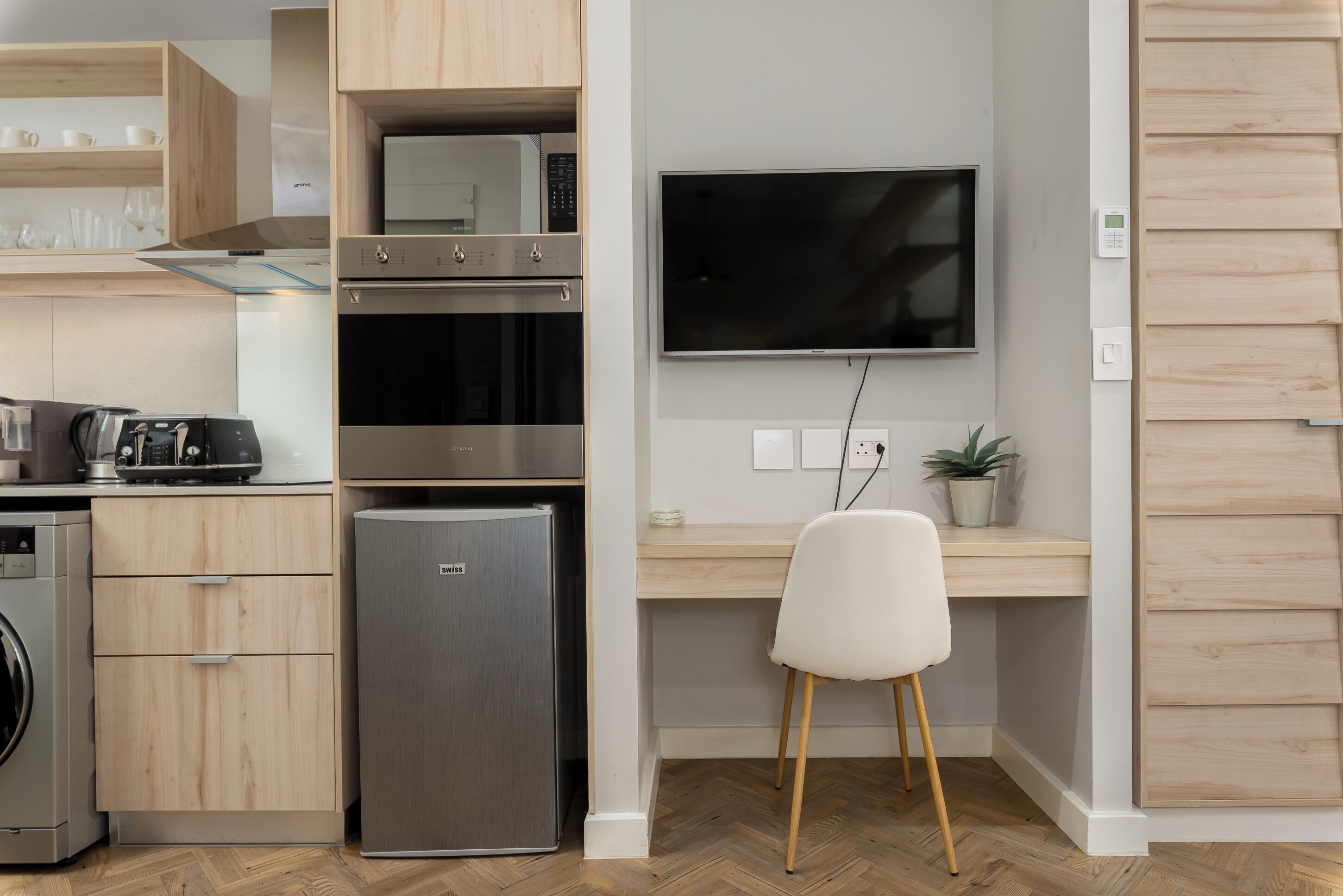 Eine moderne Küche mit Edelstahlgeräten, inklusive Backofen, Mikrowelle und Kühlschrank. Es gibt eine Holz Arbeitsplatte, einen weißen Stuhl und einen Blumentopf.