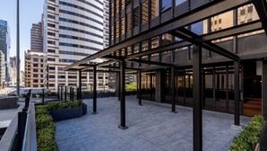 Un espace urbain moderne situé sur un toit, doté d’une zone extérieure couverte et entouré d’immeubles de grande hauteur.