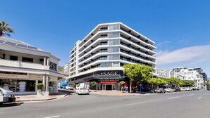 A multi-story building with a modern architectural design, featuring balconies and a storefront with a sign that reads "SAGE." - The Sage | Modern and Bright Sea Point Apartment (Cape Town)