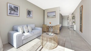 A modern living room with a sofa, round wicker coffee table, and framed artwork on the walls.