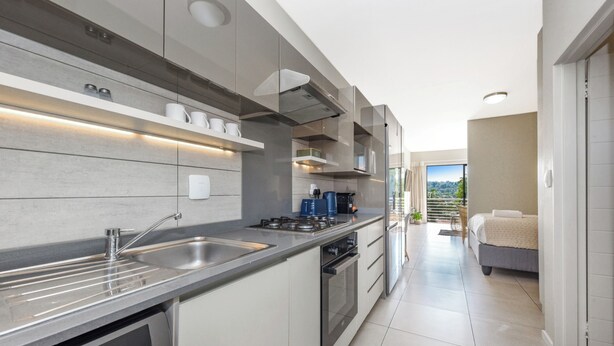 A modern kitchen with a dishwasher, stove, and sink. There is a balcony with a view of the outdoors.