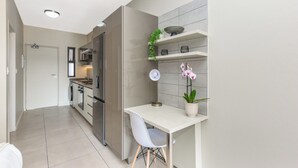 A modern kitchen with a white countertop, stainless steel appliances, and a small dining area with a white table and chair.