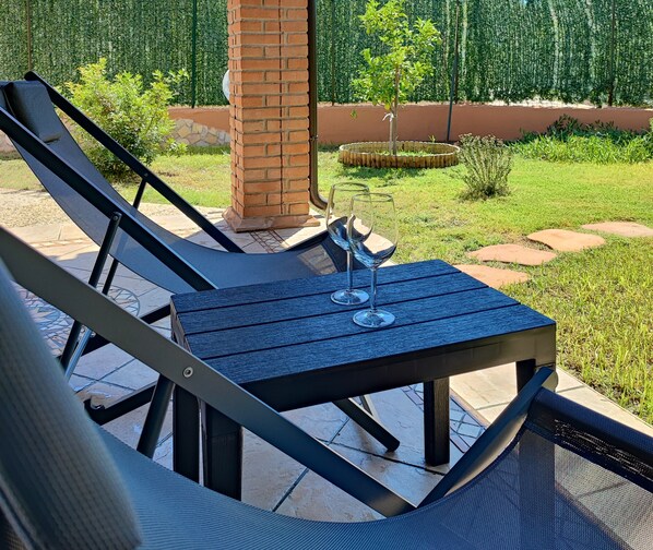 A patio area with a table and two lounge chairs, a glass of wine, and a brick pillar.
