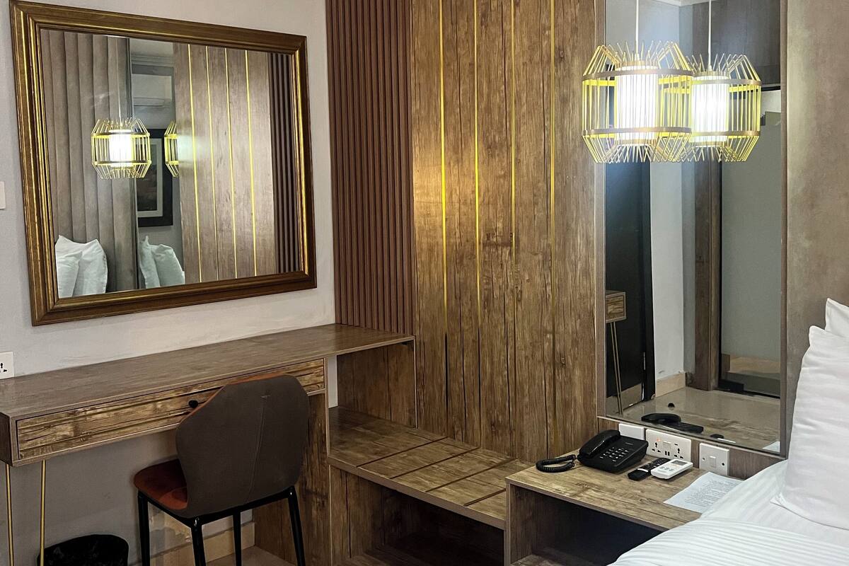 Een hotelkamer met een wand van houten panelen, een grote spiegel, een bureau met stoel, een bed en een hangende lamp.