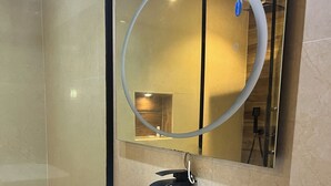 Ένα μοντέρνο μπάνιο με λευκό νιπτήρα, μαύρο πάγκο και καθρέφτη με κυκλικό πλαίσιο.