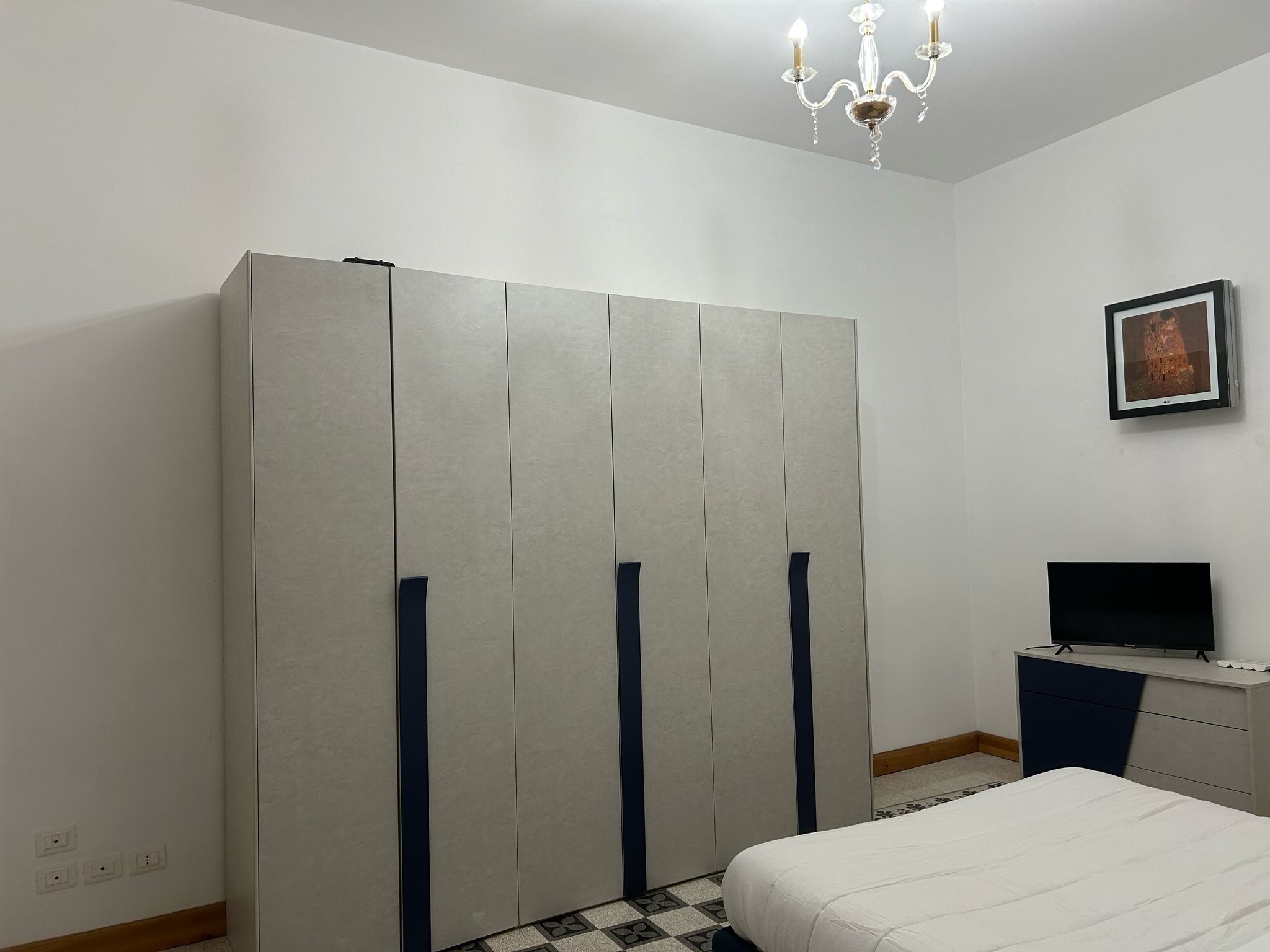 Una camera da letto con un letto, un armadio, una televisione e un lampadario.
