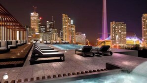 A rooftop pool area with lounge chairs and a cityscape view at night. - Central CN Tower View | 3bed 3 bath | 6 Guest | Pool | Gym | Parking (Toronto)