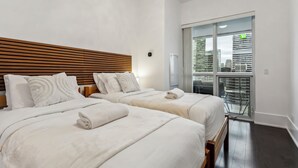 A hotel room with two beds, a wooden headboard, white bedding, and a view of the city through a sliding glass door. - Central CN Tower View | 3bed 3 bath | 6 Guest | Pool | Gym | Parking (Toronto)