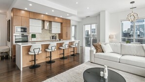 A modern kitchen with a central island, bar stools, and a city view through large windows. - Central CN Tower View | 3bed 3 bath | 6 Guest | Pool | Gym | Parking (Toronto)
