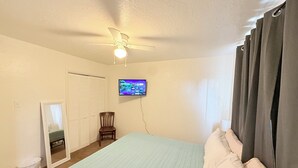 Ein Schlafzimmer mit Bett, Deckenventilator, Fernseher, Sessel, Spiegel und Kleiderschrank.