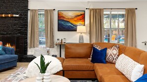 Una sala de estar moderna con chimenea, un ventanal con cortinas, un sofá y un cuadro en la pared.