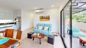 Un salon moderne avec un canapé bleu clair, une table basse en bois et une porte en verre donnant sur un balcon extérieur.