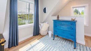 A room with a large window, a blue dresser, a white wall, and a blue and white striped rug.